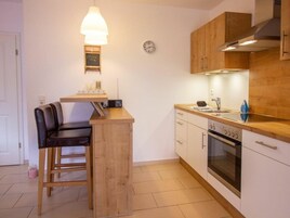 A compact kitchen with a wooden bar counter, a built-in oven, and a clock on the wall.