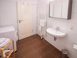 Un baño con un lavamanos blanco, un perchero, una puerta blanca y un pequeño cubo de basura.