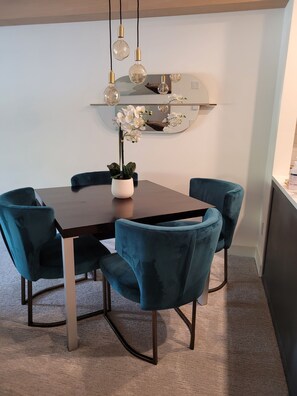 A dining area with a dark wooden table, four teal chairs, a potted orchid, and a wall-mounted light fixture. - Creekside Gondola, pool, hot tub, BBQ, & free parking! (Whistler)