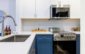 A kitchen with white cabinets, a stainless steel range, and a microwave. - Creekside Gondola, pool, hot tub, BBQ, & free parking! (Whistler)