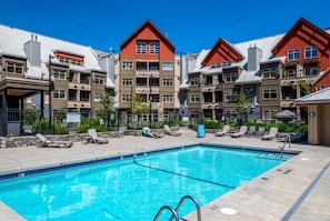 A swimming pool with lounge chairs and a building with red roofs and balconies. - Creekside Gondola, pool, hot tub, BBQ, & free parking! (Whistler)