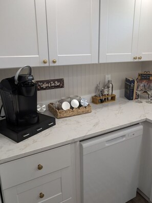 Eine Küche mit weißen Schränken, einer Kaffeemaschine, einem Schild für die Tee-Bar und einem Tellergestell.