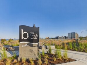 A sign for 'The Beach Lands' with a modern building in the background. - Brand New Luxury Retreat in Scenic Royal Bay (Metchosin)