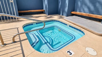 A small, rectangular swimming pool with a metal ladder, a wooden bench, and a tiled edge.