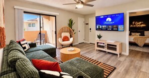 A modern living room with a sectional sofa, a round coffee table, and a television mounted on the wall displaying Paramount+ content. - Next to ASU • King Bed • Arcade • Pool/Spa • Sleeps 8 • Pets • 65" TV • W/D (Tempe)
