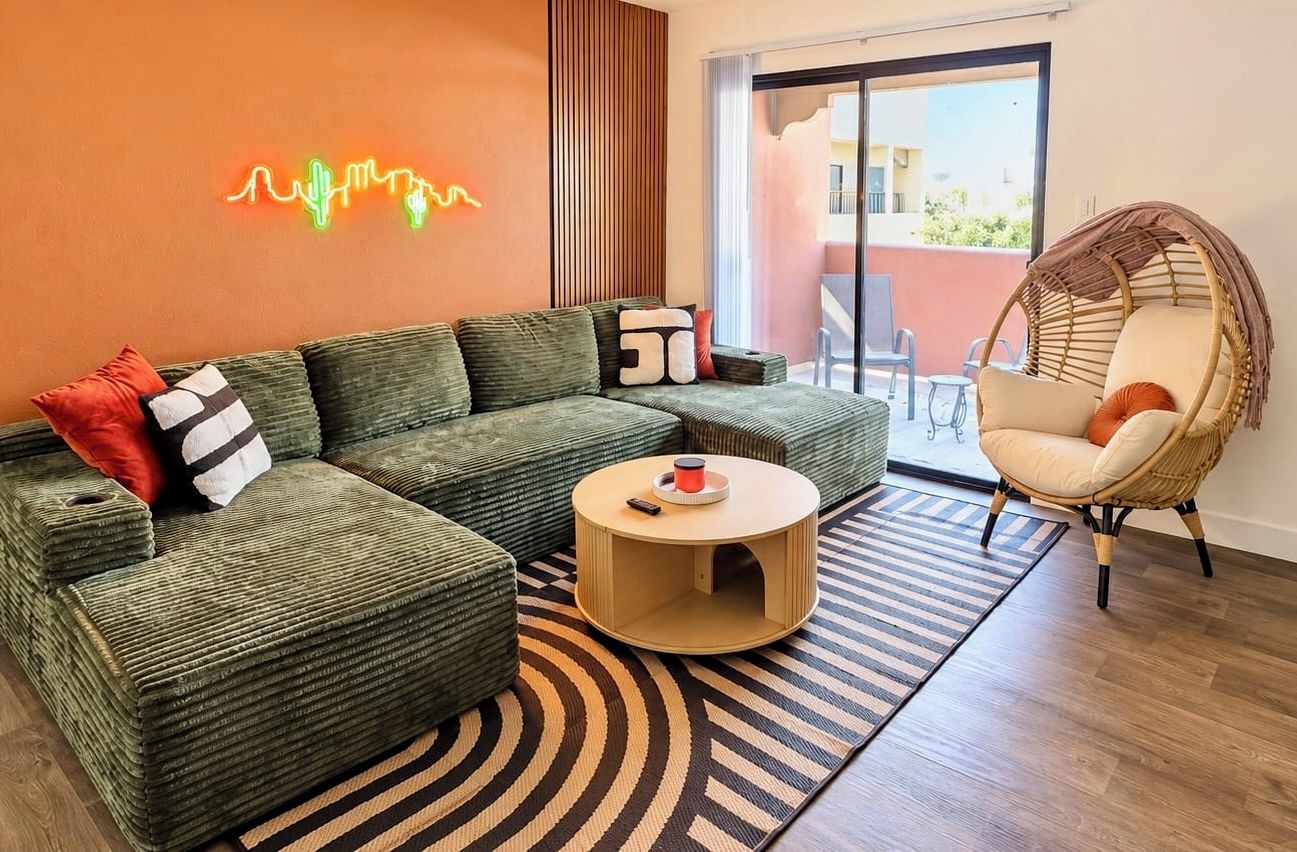 Una sala moderna con un sofá modular, una mesa de centro redonda y una silla de mimbre.