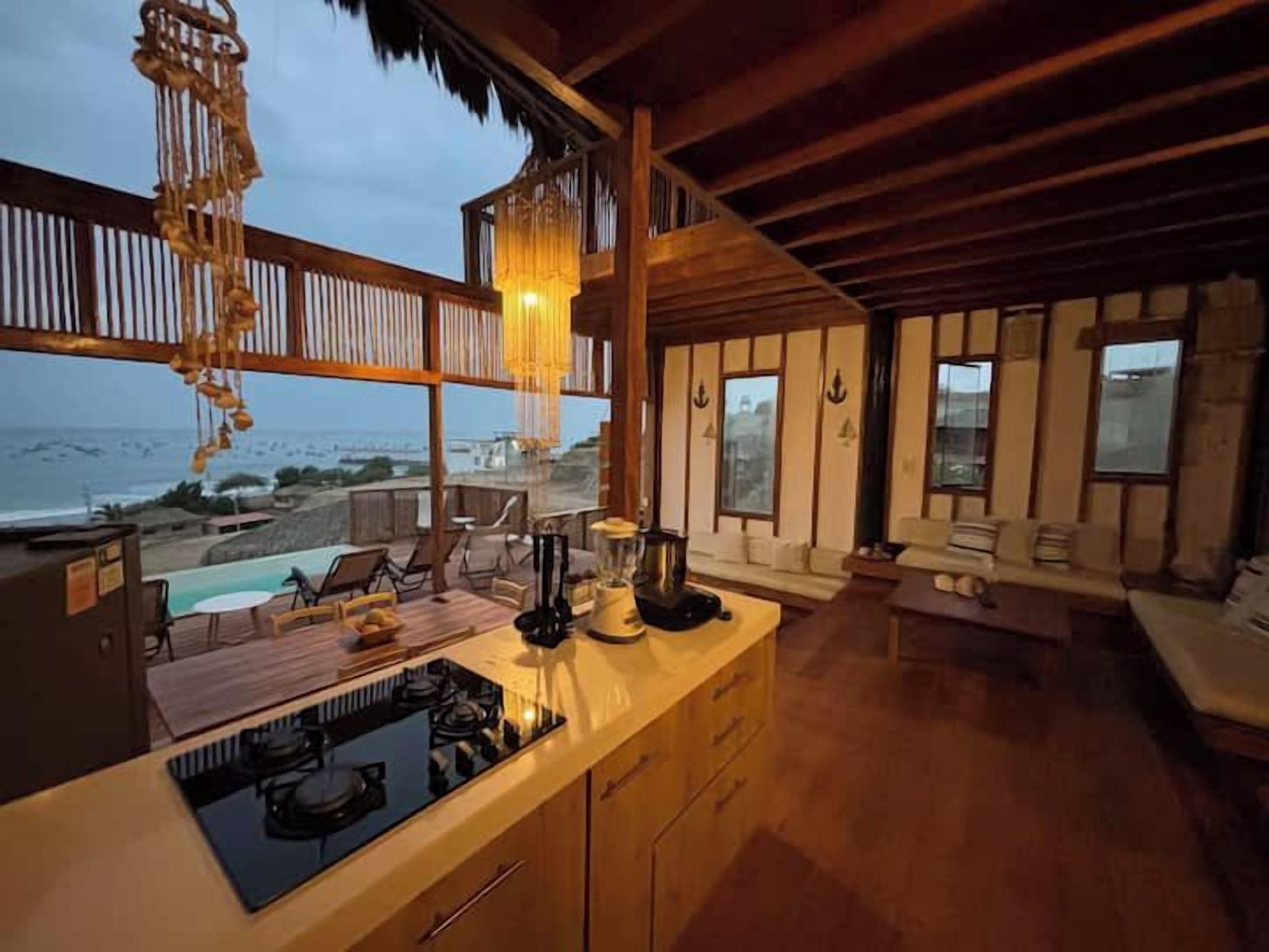 Cozinha com vista para o oceano, móveis de madeira e luminária pendente.