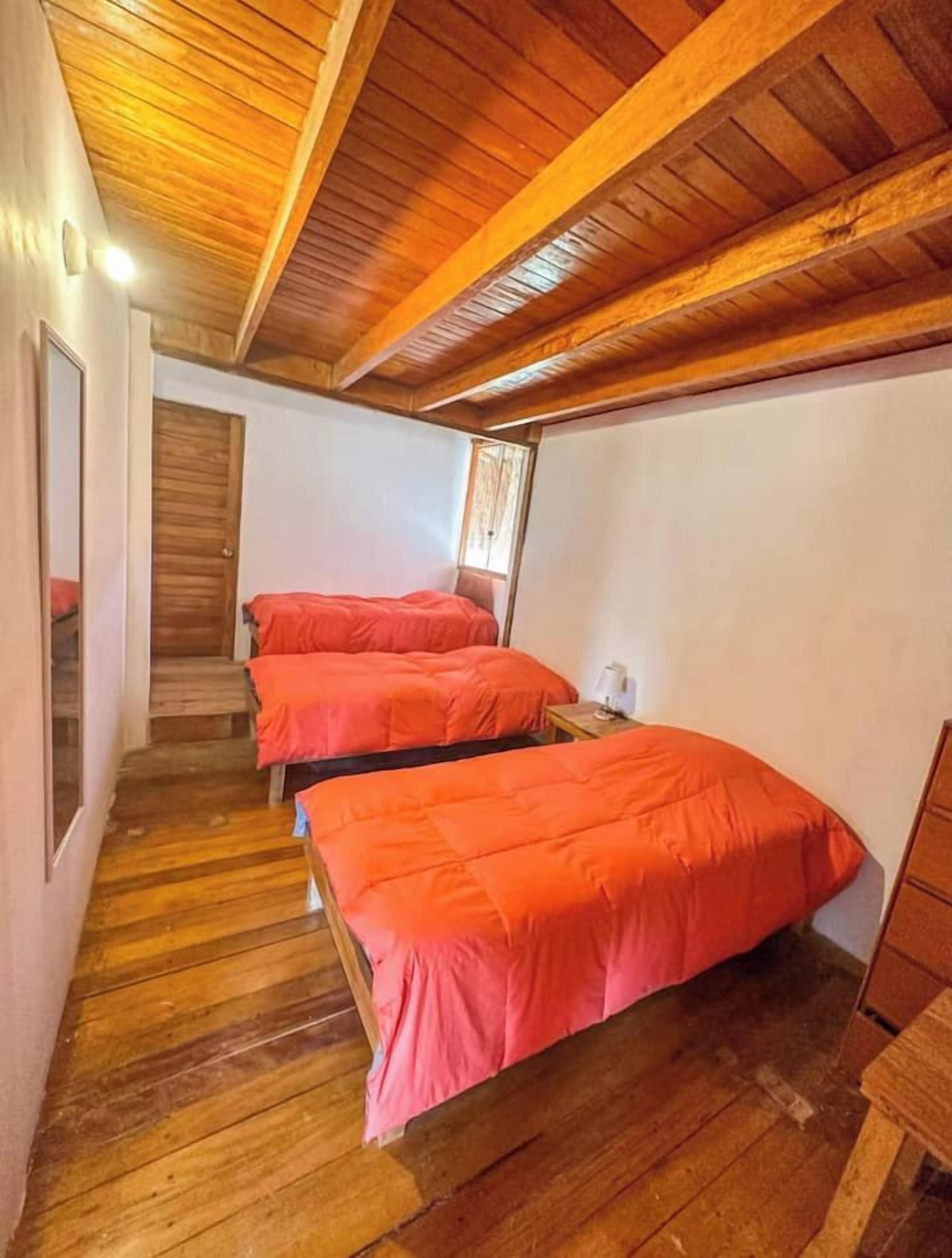A room with wooden floors and a sloped ceiling, featuring three beds with orange bedding.