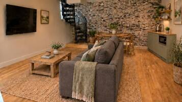 A modern living room with a stone wall, a gray sofa, wooden coffee table, and a staircase.