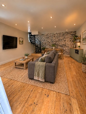 Una sala de estar moderna con pared de piedra, un sofá gris, una mesa de centro de madera y una escalera.