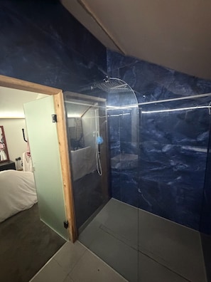 Une salle de bain avec une douche à parois de verre, une porte en bois et un mur en marbre.