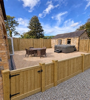 Un patio con valla de madera, una mesa con sillas y un jacuzzi.
