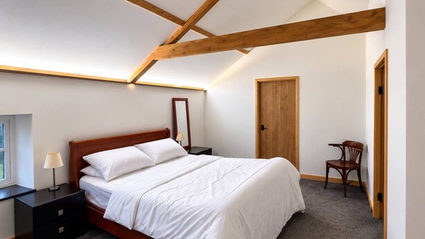 Quarto com cama de madeira, mesa de cabeceira, cadeira e porta.