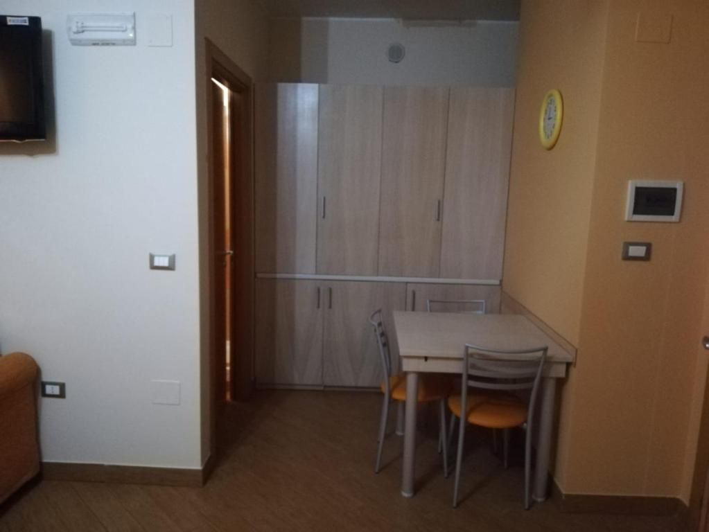 A compact room with a kitchenette, a dining area with two chairs, and a television mounted on the wall.