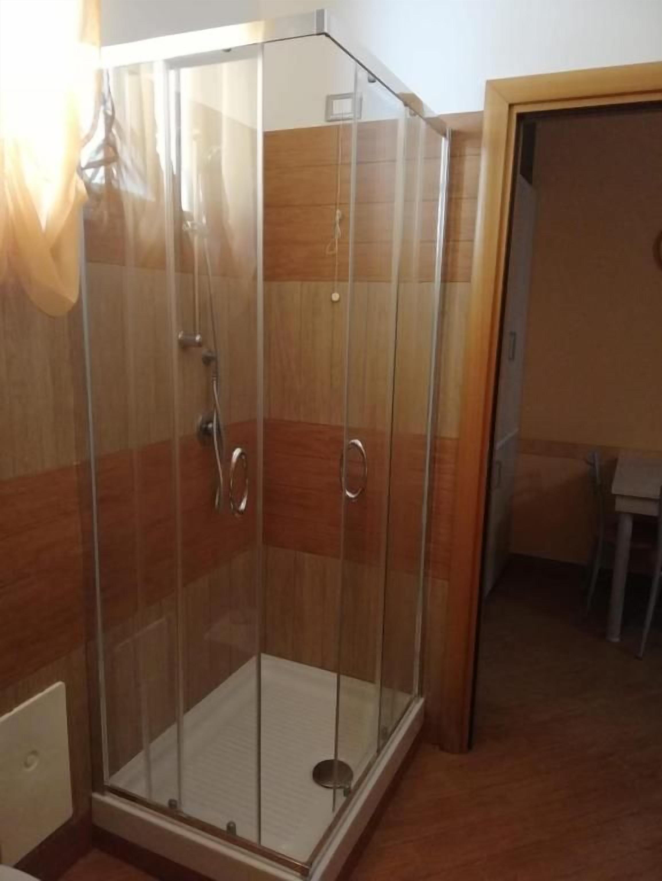 Eine gläserne Dusche mit Holzboden und einer Tür zum Badezimmer.