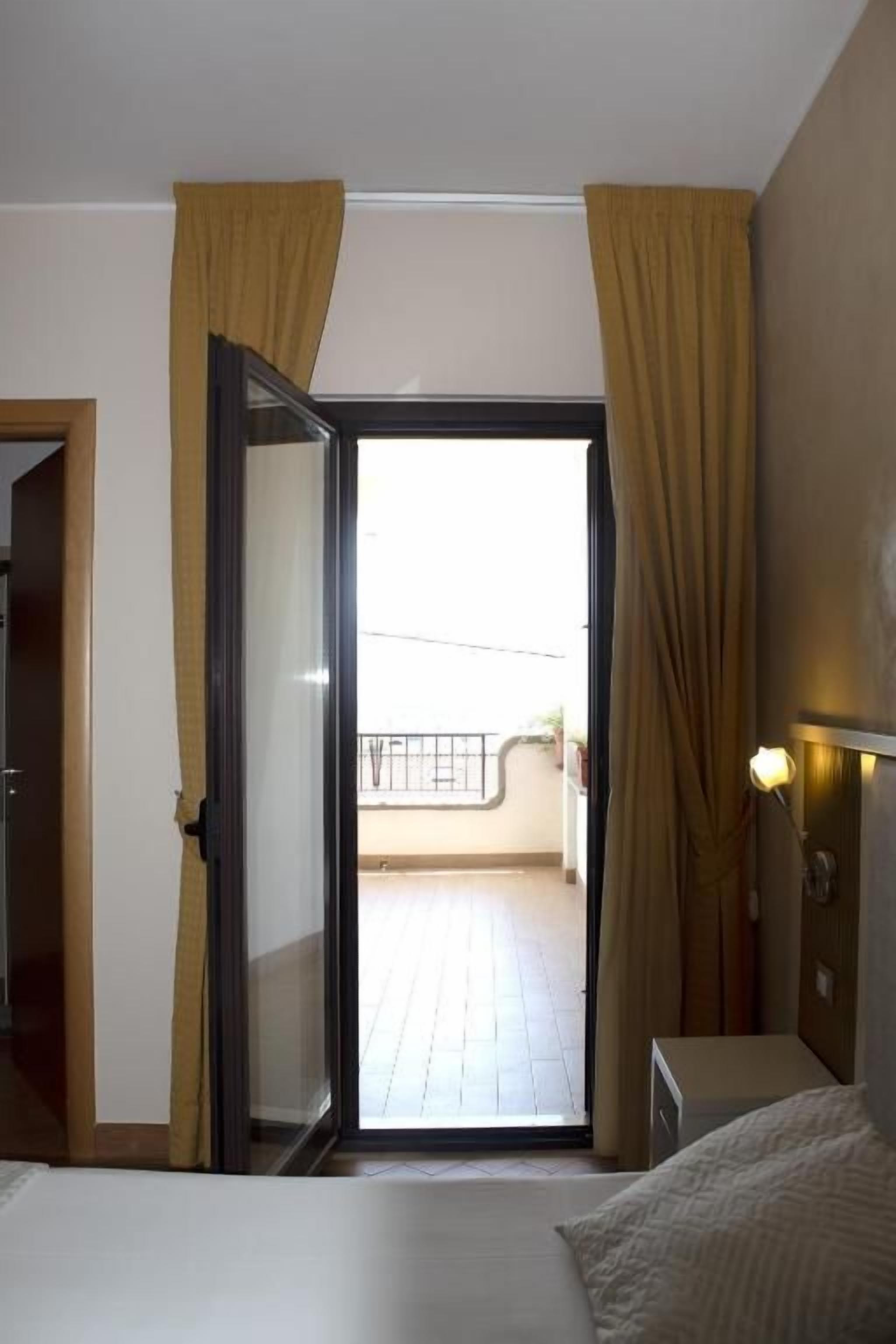 Une chambre d’hôtel avec un lit, une porte donnant sur un balcon et une table de chevet avec une lampe.