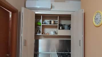 Una cocina compacta con estufa a gas, repisas con utensilios de cocina y un reloj en la pared.