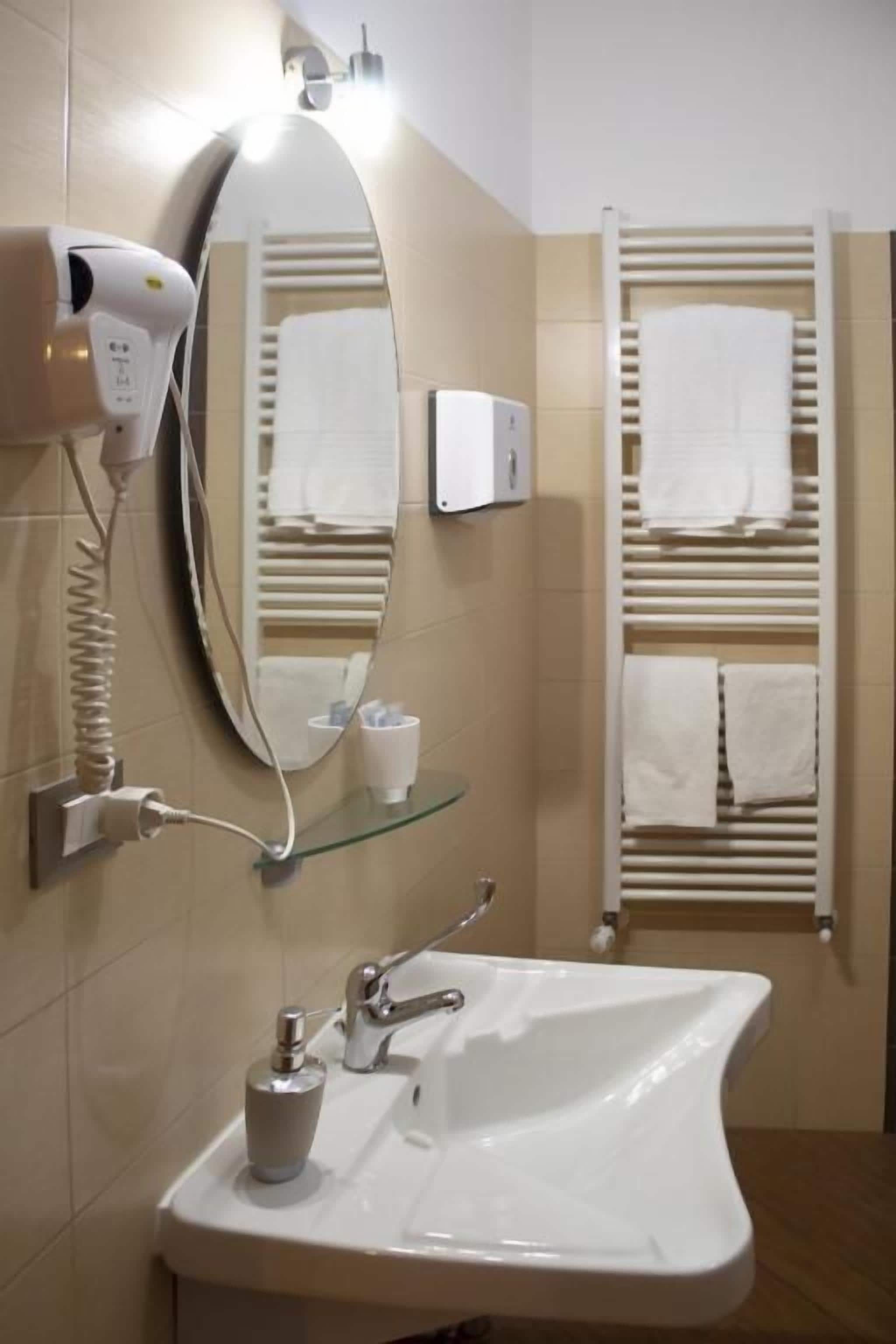 Une salle de bain équipée d’un lavabo, d’un miroir, d’un sèche-cheveux, d’un porte-serviettes et d’une étagère en verre.