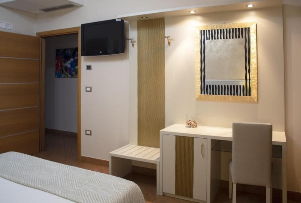 A bedroom with a bed, a desk, a chair, a television, and a mirror.