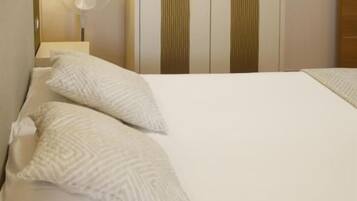 Una cama bien hecha con almohadas, una lámpara de noche y un ventilador de pared.