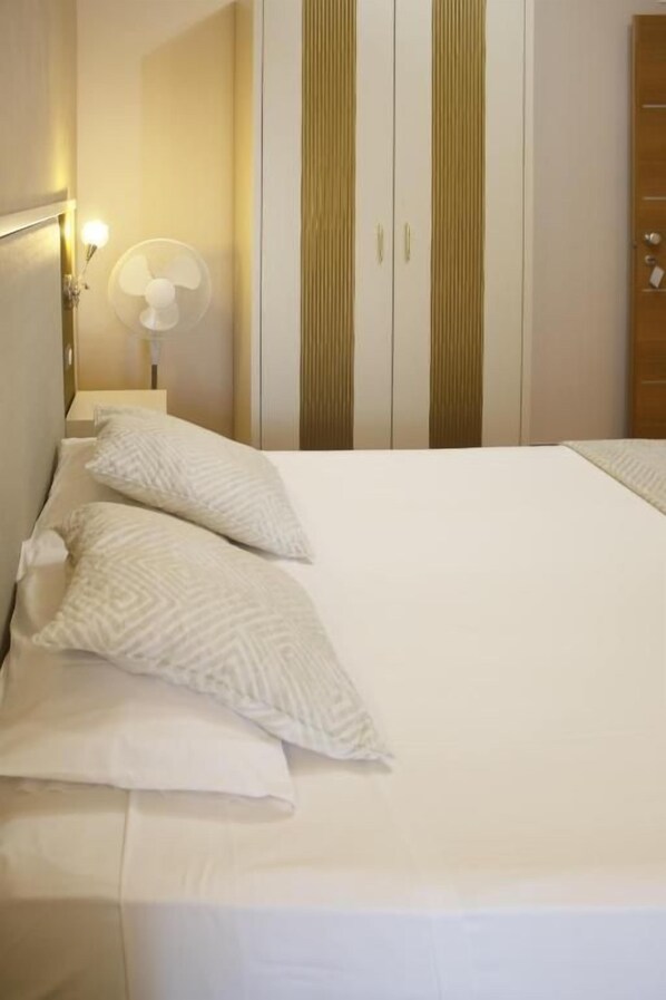 A neatly made bed with pillows, a bedside lamp, and a wall-mounted fan.