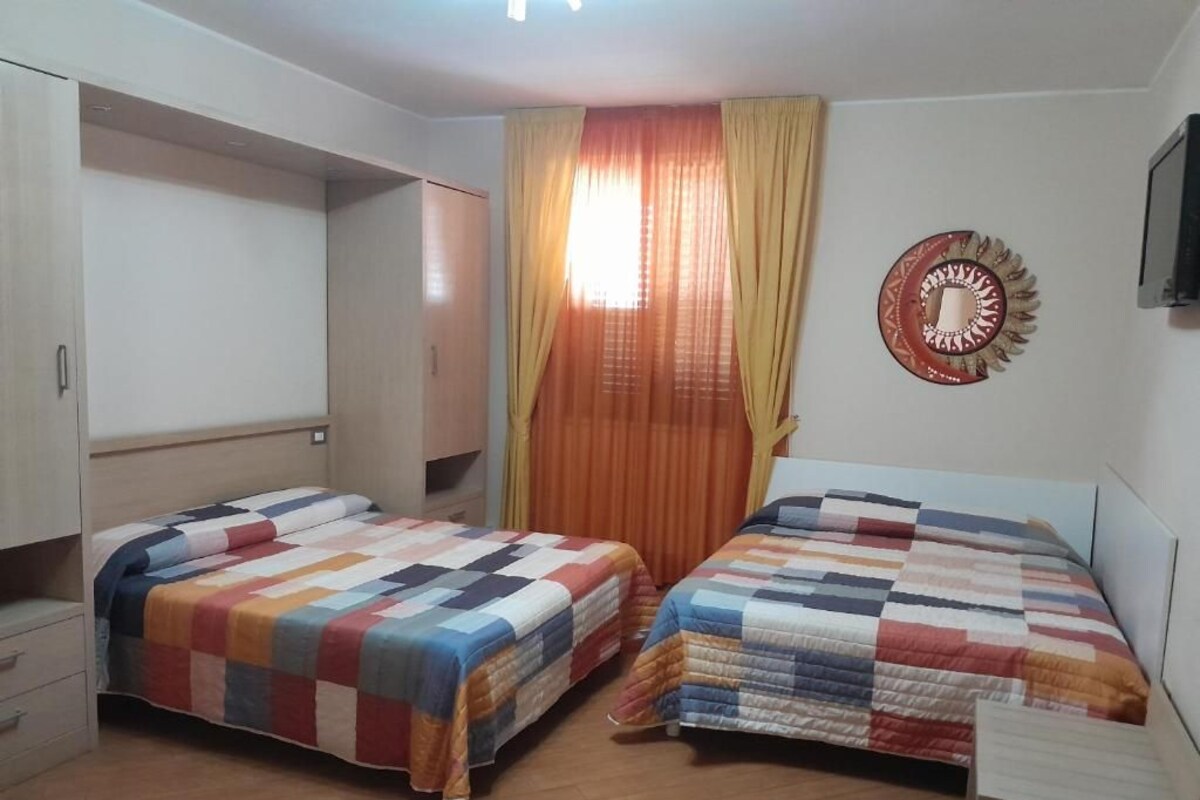 A bedroom with two beds, a wardrobe, a mirror, and a window with curtains.