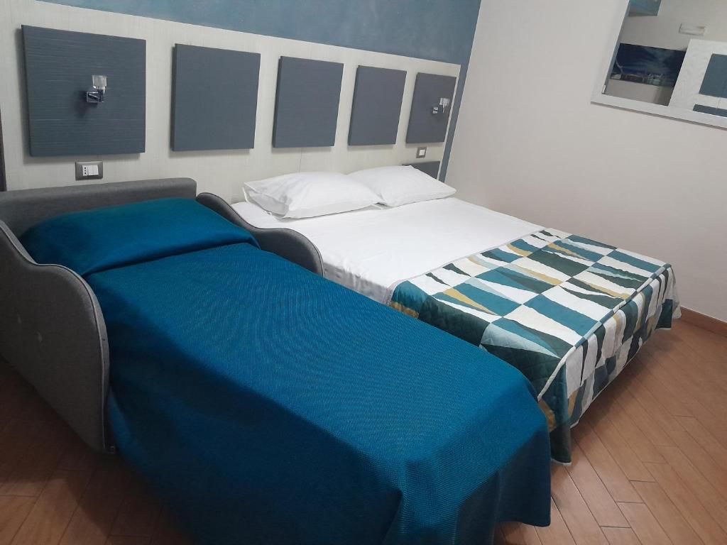 Quarto de hotel com duas camas, um sofá cinzento e uma televisão fixada na parede.