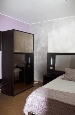 A hotel room with a bed, a wardrobe, and a nightstand.