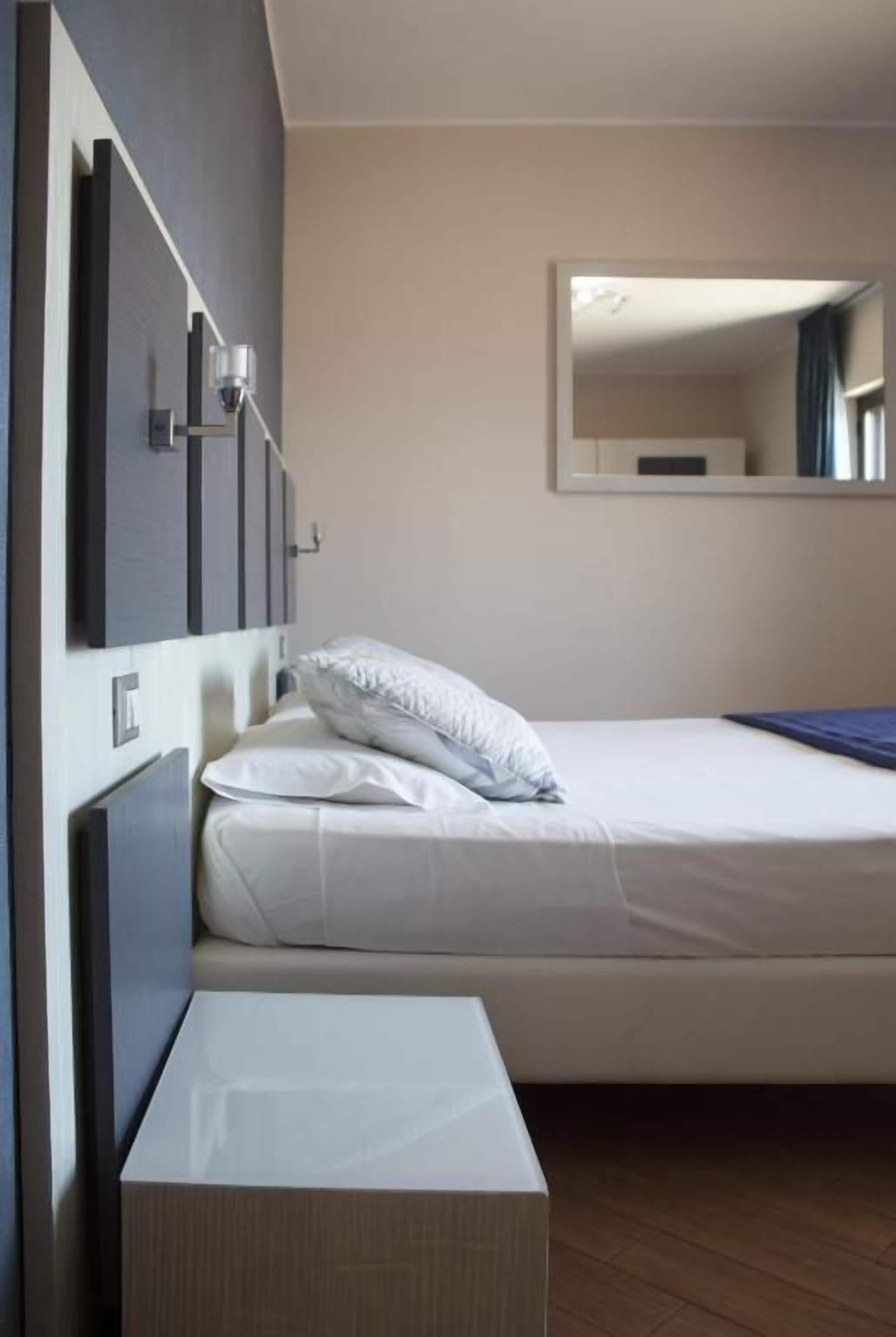 Una cama individual con cabecera, una mesita de noche y un espejo fijado a la pared.
