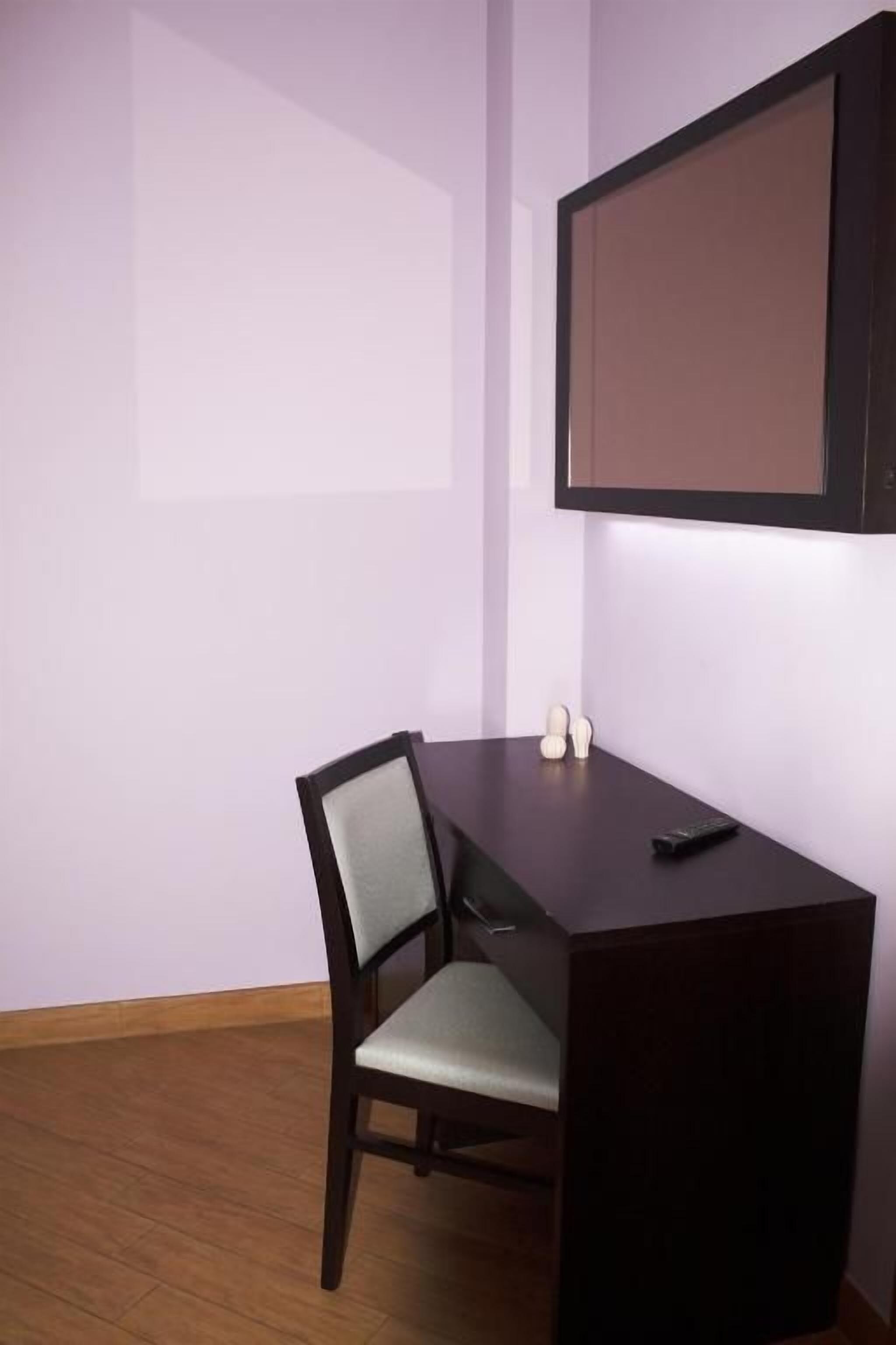 Una habitación con un escritorio de madera oscura, una silla y un televisor instalado en la pared.