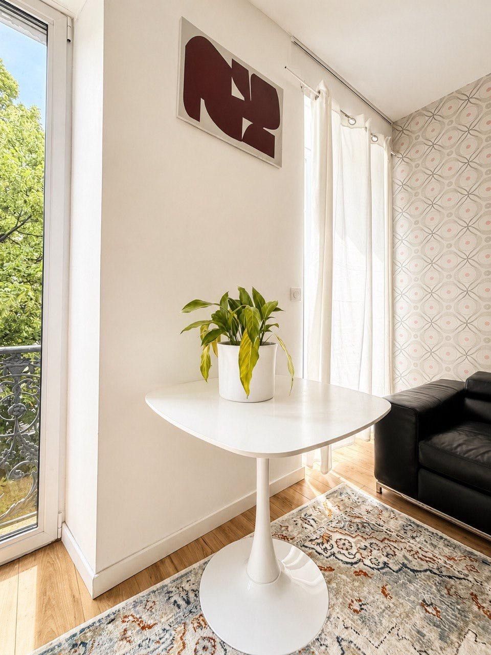 Ett rum med ett vitt, runt bord, en krukväxt, en svart soffa och en mönstrad matta.