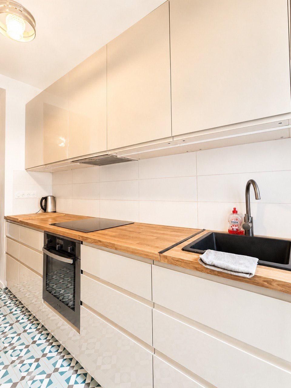 Una cocina moderna con armarios blancos, encimera de madera, horno empotrado y salpicadero de azulejos.