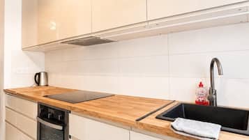 Una cocina moderna con armarios blancos, encimera de madera, horno empotrado y salpicadero de azulejos.