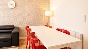 Un comedor con una mesa blanca y sillas rojas, un sofá negro, papel tapiz estampado, una obra de arte azul y una lámpara.