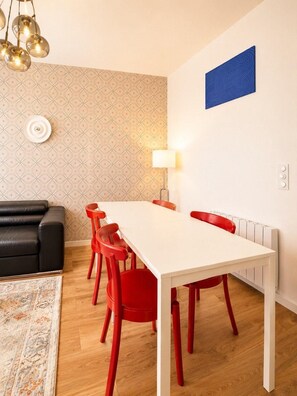 En matplats med ett vitt bord och röda stolar, en svart soffa, mönstrat tapet, ett blått konstverk och en lampa.