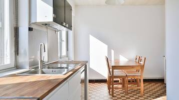 Una cocina con encimera de madera, pileta de acero inoxidable y comedor con piso a cuadros, mesa y sillas.