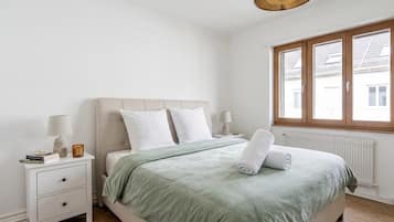 Un dormitorio con cama, mesita de noche, lámpara y ventana con vistas a edificios.