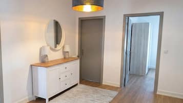 Un pasillo con un armario blanco, un espejo, una alfombra y una puerta que da a otra habitación.