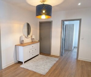 Un pasillo con un armario blanco, un espejo, una alfombra y una puerta que da a otra habitación.