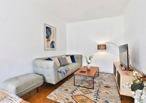 Una sala de estar con sofá, mesa de centro, mueble para televisor e iluminación instalada en la pared.