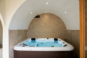 A hot tub in a room with a stone wall and a wooden floor. - Kalimera - Jacuzzi & Sauna (Oullins-Pierre-Bénite)