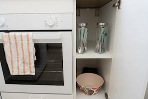 A kitchen with a microwave, oven, and a shelf with jars and utensils.