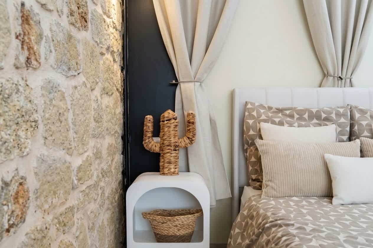 A bedroom with a stone wall, a cactus decoration, a bed with patterned bedding, and curtains tied back.