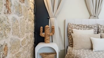 A bedroom with a stone wall, a cactus decoration, a bed with patterned bedding, and curtains tied back.