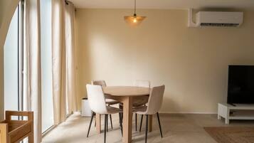 Een eetgedeelte met een ronde tafel, stoelen, een hanglamp en een televisie op een standaard.