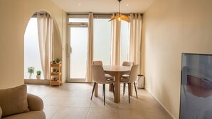 Uma sala de estar moderna com sofá, mesa de jantar com cadeiras, televisão e estante de livros com plantas.