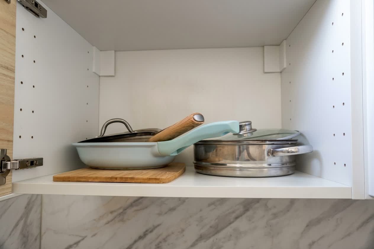 A kitchen with a white countertop, a blue pan with a wooden handle, and a stainless steel pot on a wooden cutting board.