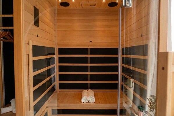 A sauna with wooden walls and a bench, towels on the bench, and a small plant on the right. - Kalimera - Jacuzzi & Sauna (Oullins-Pierre-Bénite)