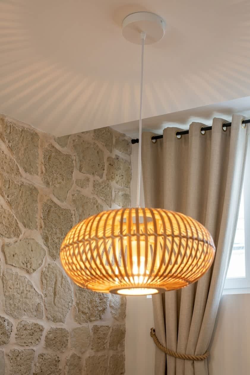 Une pièce avec un mur en pierre, un luminaire suspendu et un rideau.