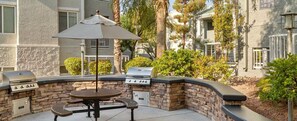 An outdoor patio with a round table, two barbecue grills, and an umbrella. - Wyndham Tropicana 2 bdrm in Las Vegas for F1 weekend w/ outdoor pool and hot tub (Las Vegas)
